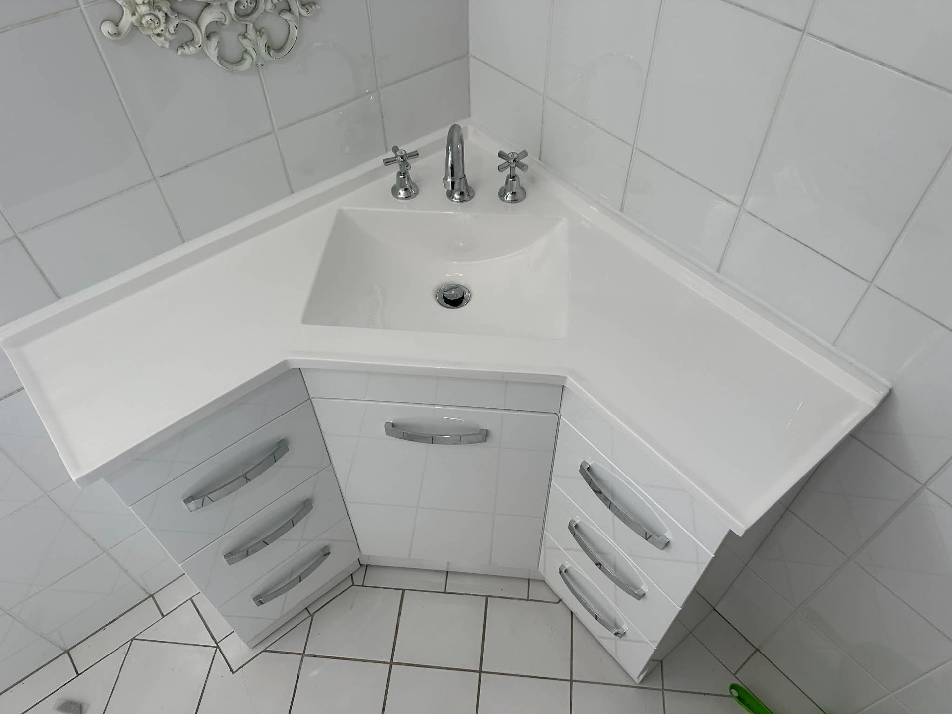 White corner bathroom vanity with sink, chrome faucet, and mirrored cabinet doors on tiled floor.