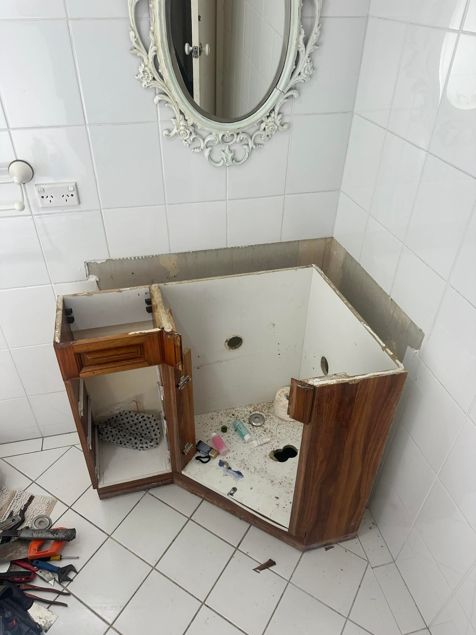 Bathroom vanity cabinet under repair with tiles removed and tools on the floor