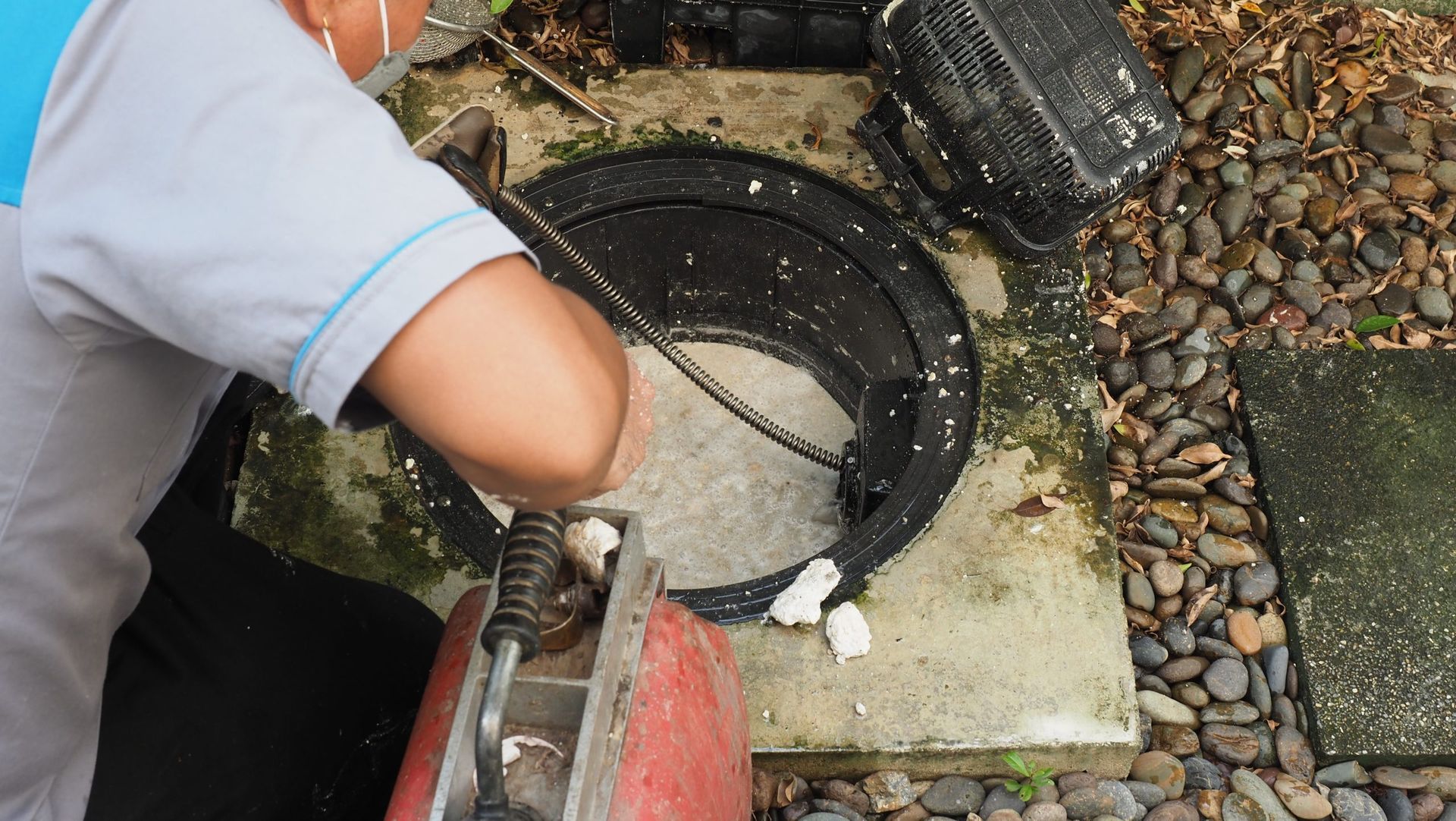 A worker using equipment to repair a concrete manhole cover outdoors.