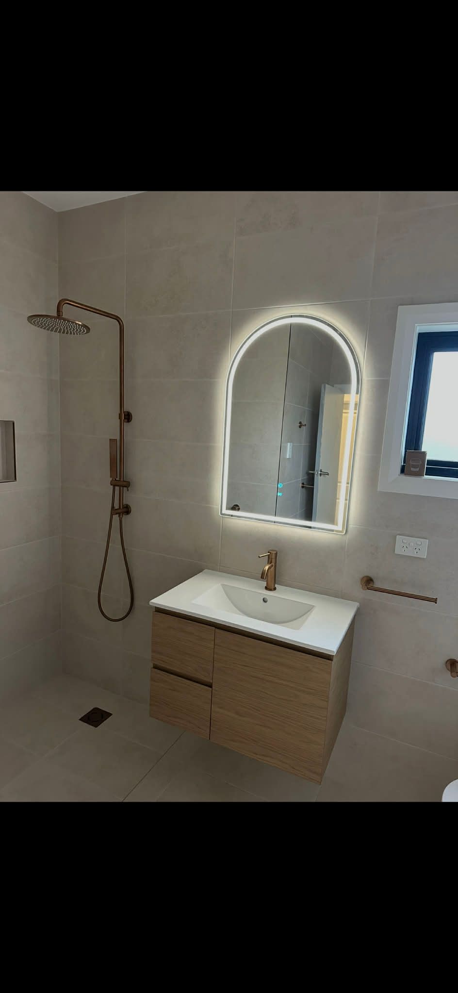 Modern bathroom with arched mirror, wall-mounted sink, shower, and window