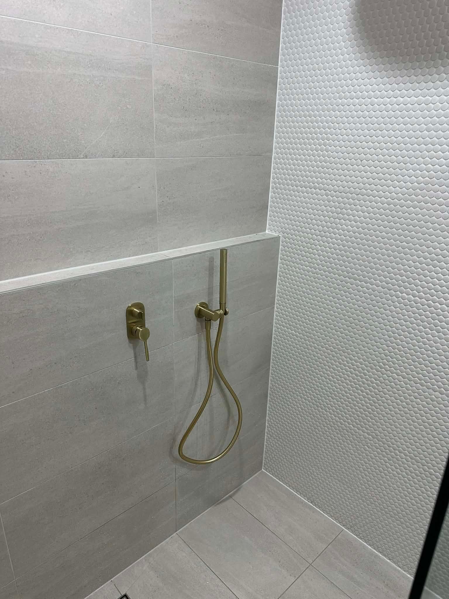 Bathroom shower area with wall-mounted brass fixtures and a flexible handheld shower hose.