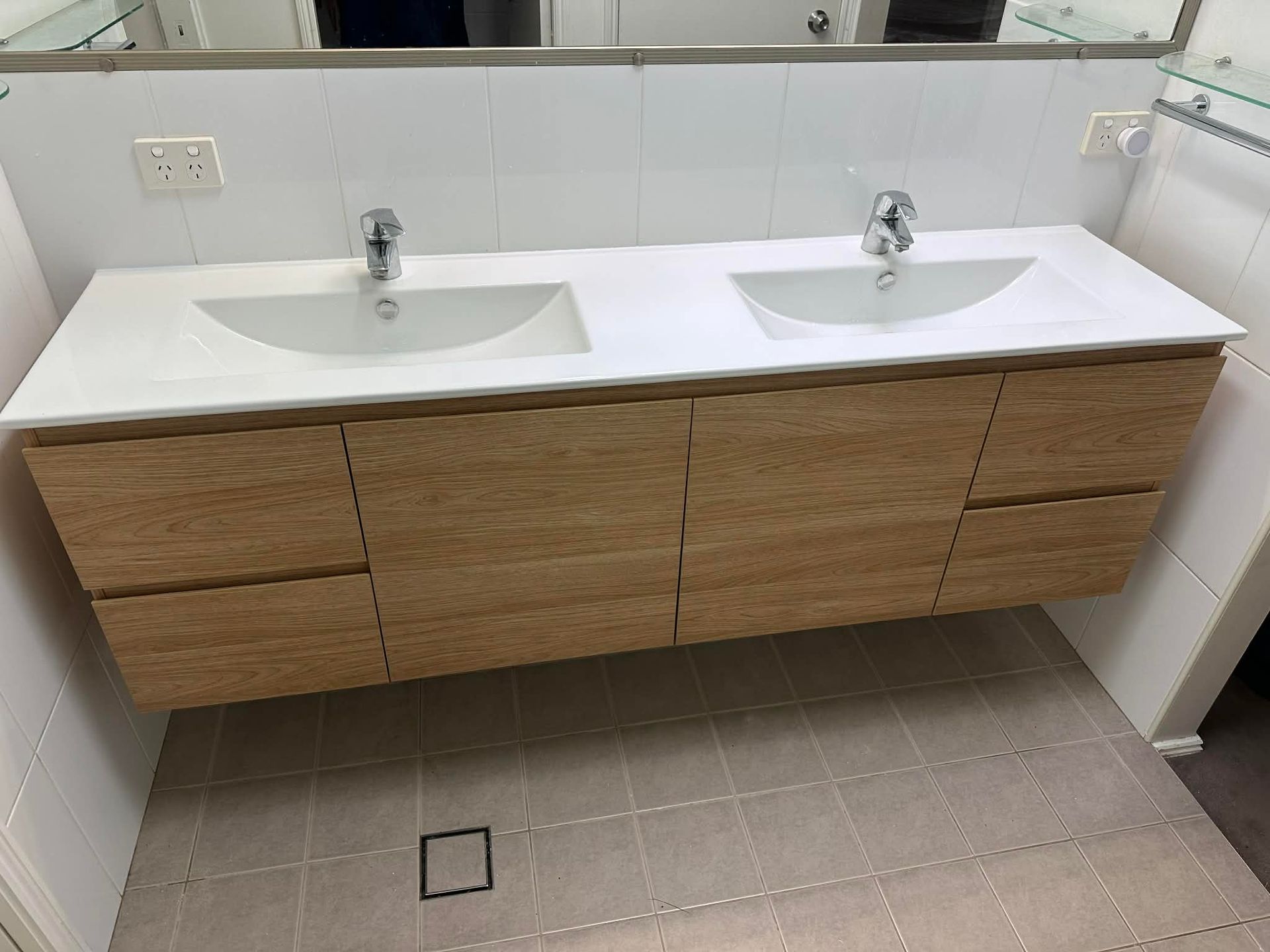 Modern double-sink vanity with wood cabinets and a white countertop in a tiled bathroom
