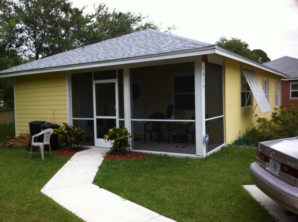 A yellow house with a screened in porch and a car parked in front of it