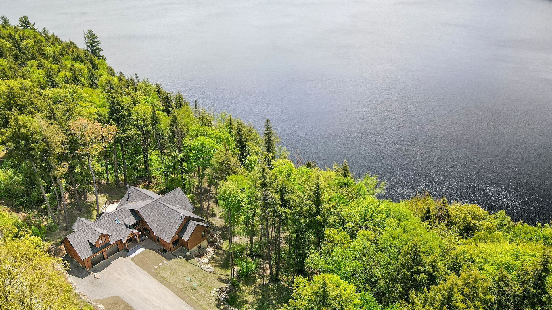 A lakeside house nestled among bright green trees beside calm dark water.