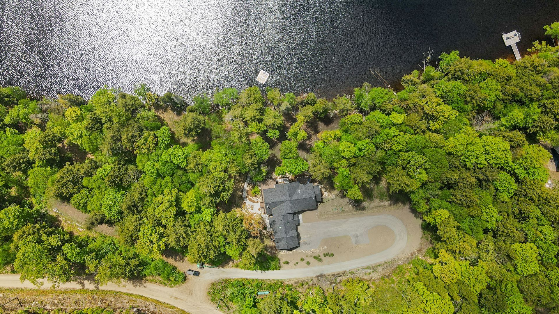 Aerial view of a winding dirt road beside dense green trees and dark water