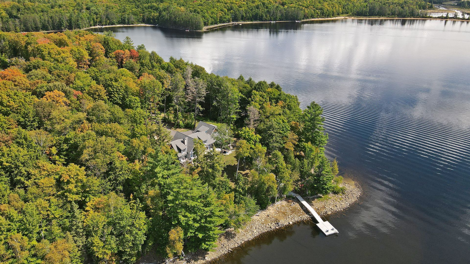 An aerial view of a house on a small island in the middle of a lake surrounded by trees.