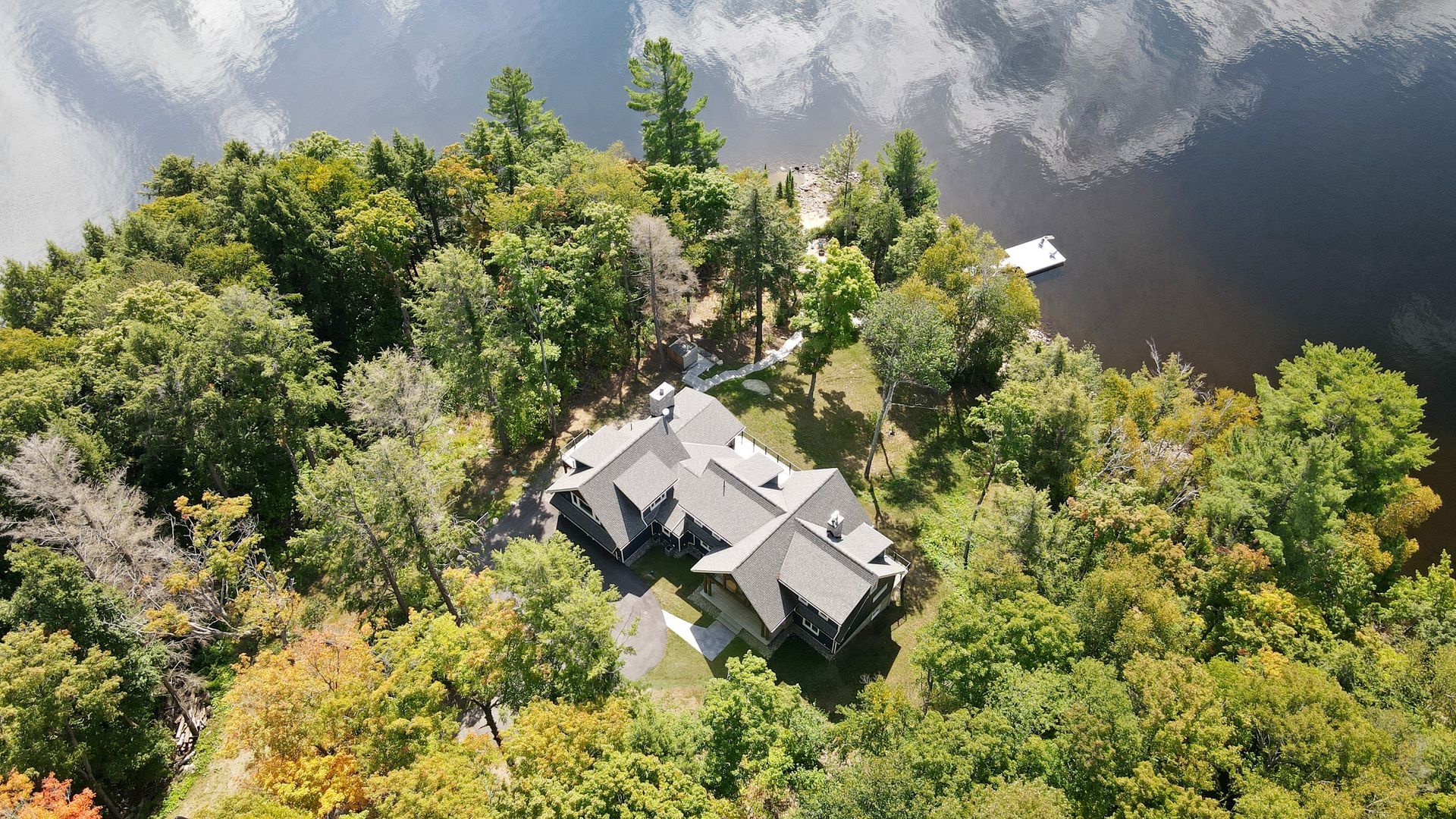 An aerial view of a house on a small island in the middle of a lake surrounded by trees.