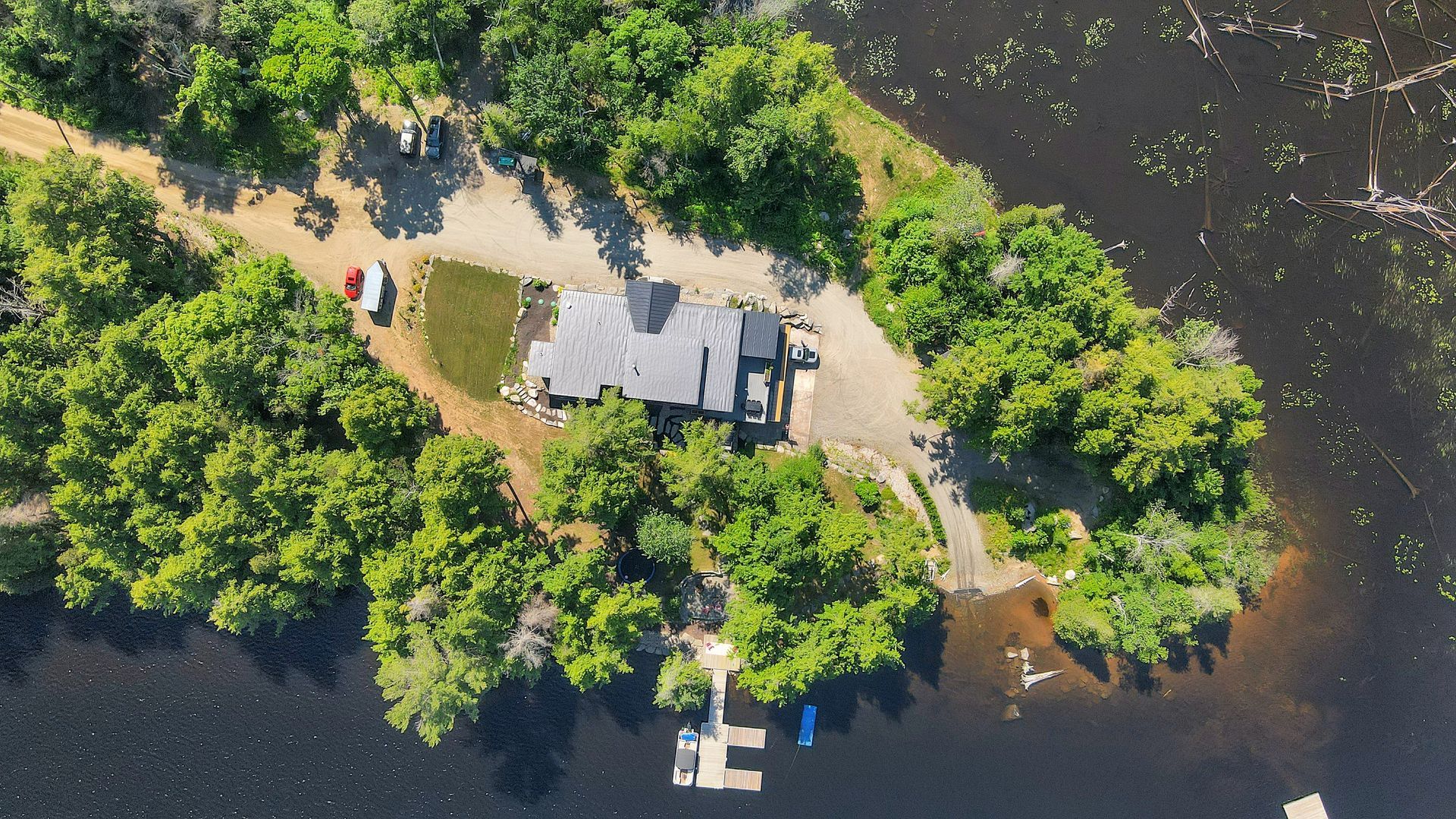 An aerial view of a house on a small island in the middle of a lake surrounded by trees.