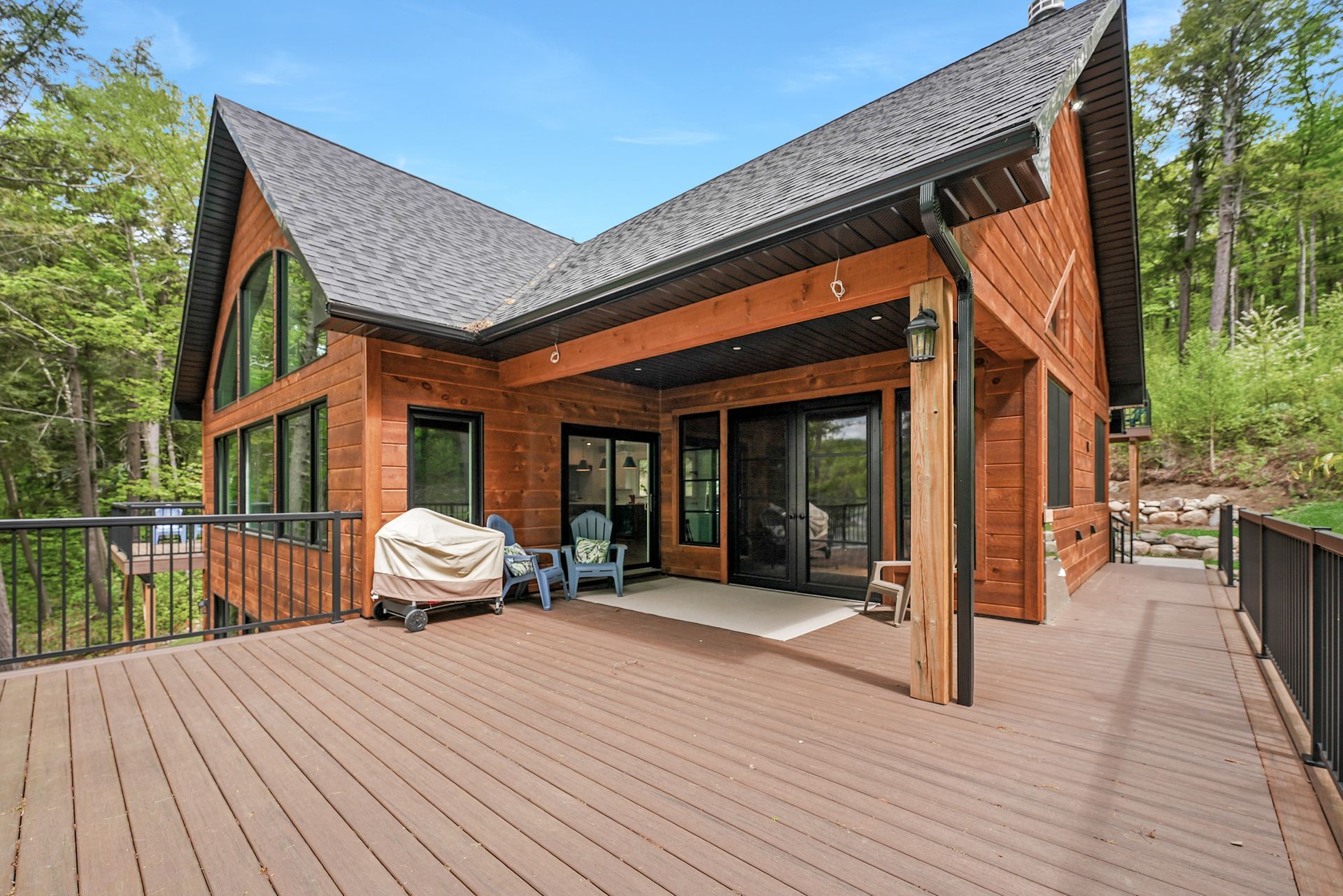 Modern wood cabin with large deck and outdoor seating in a forest setting
