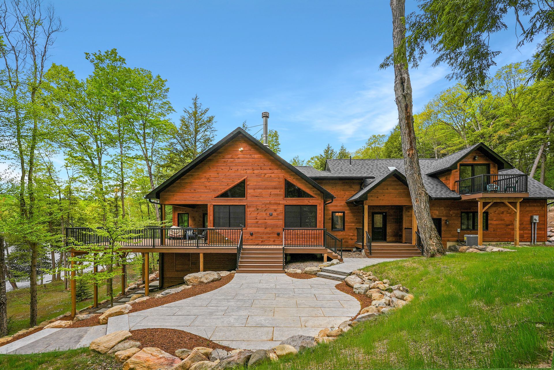Wooden cabin-style home with stone accents, a stone driveway, and trees in a green wooded setting