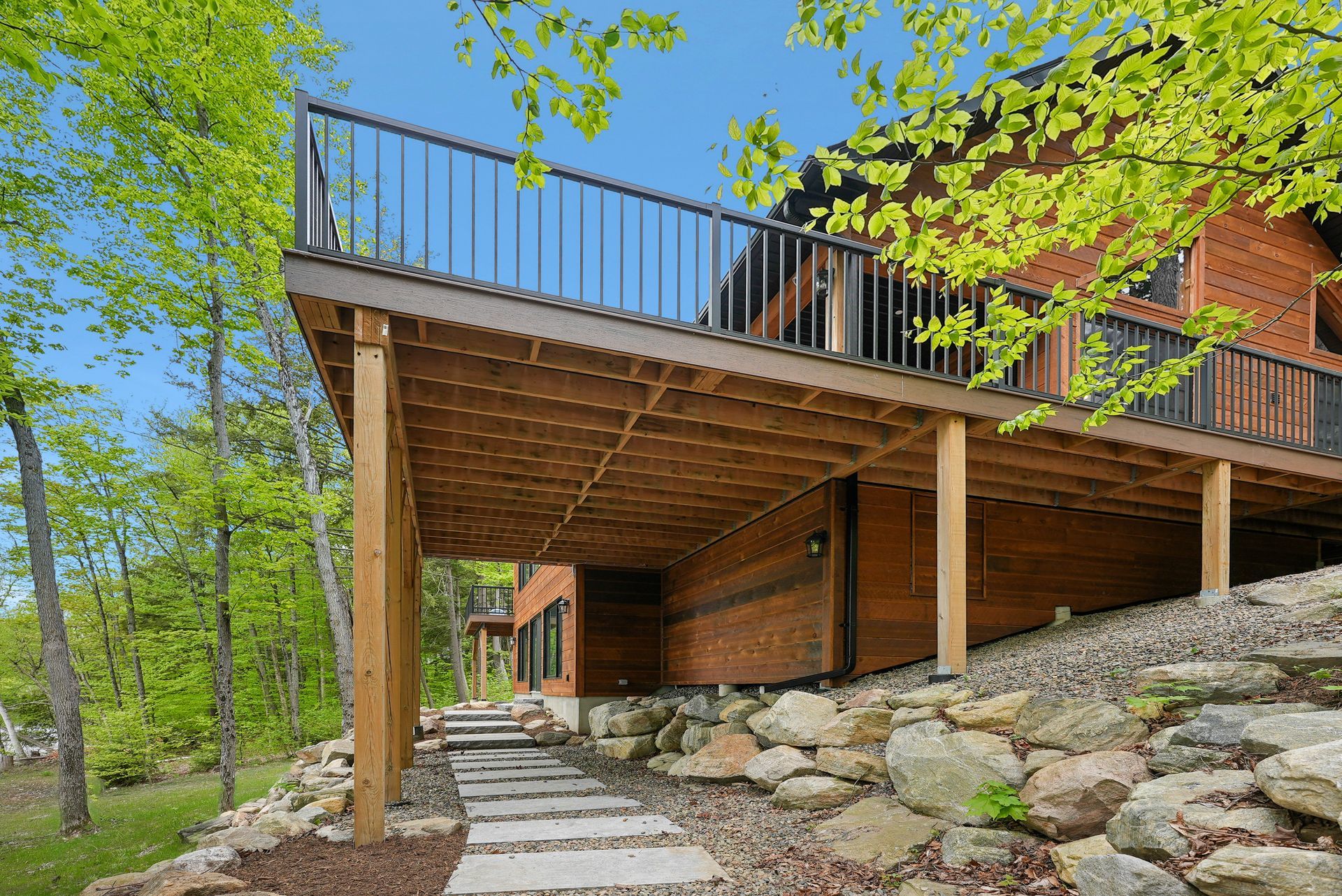 Wooden deck and walkway on a house with stone landscaping and green trees