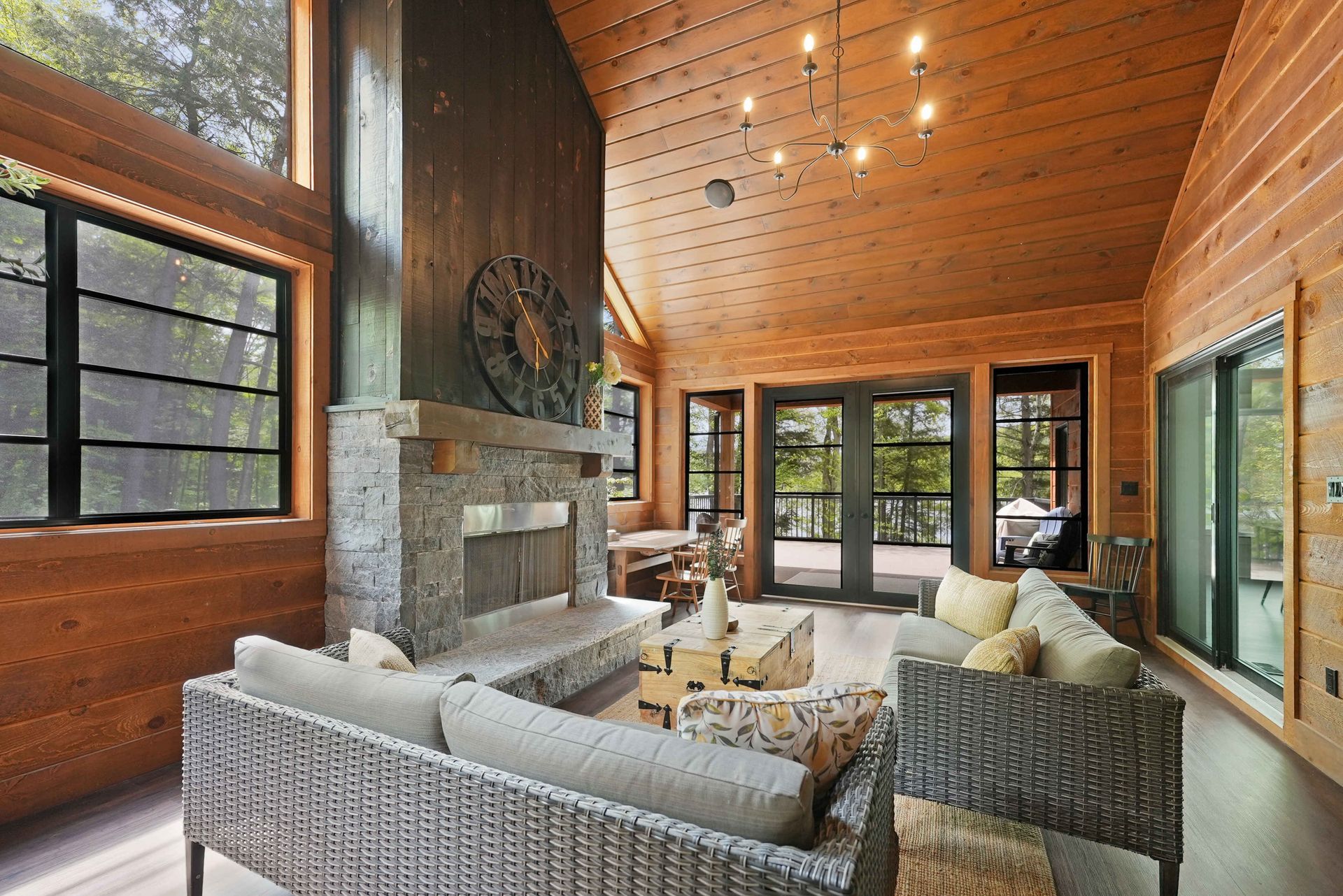 Cozy modern living room with vaulted wood ceiling, stone fireplace, and large windows overlooking greenery