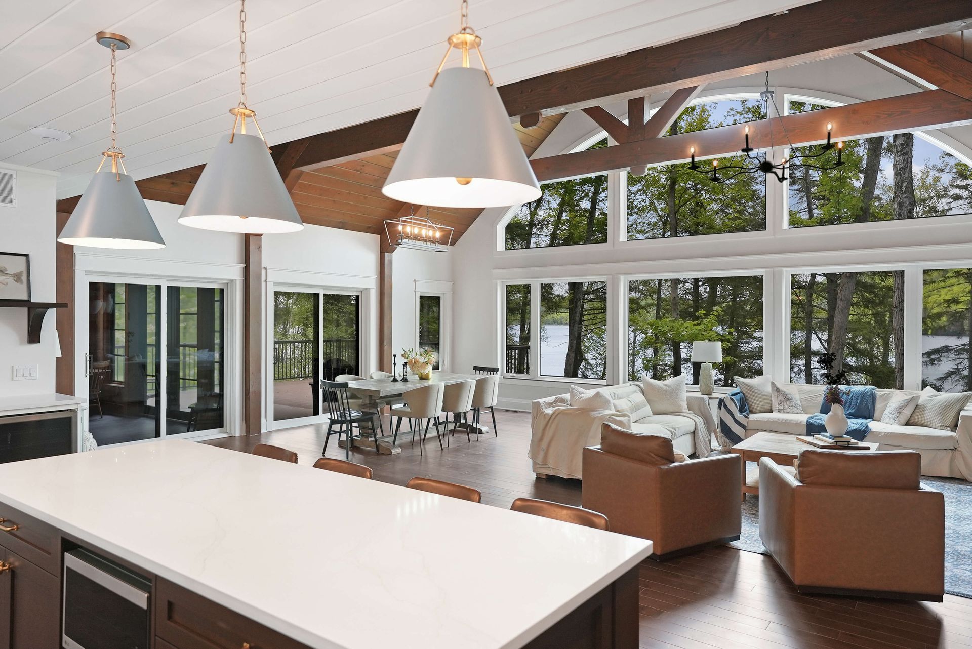 Bright open living room with white vaulted ceiling, large windows, and brown sofas beside a kitchen island.