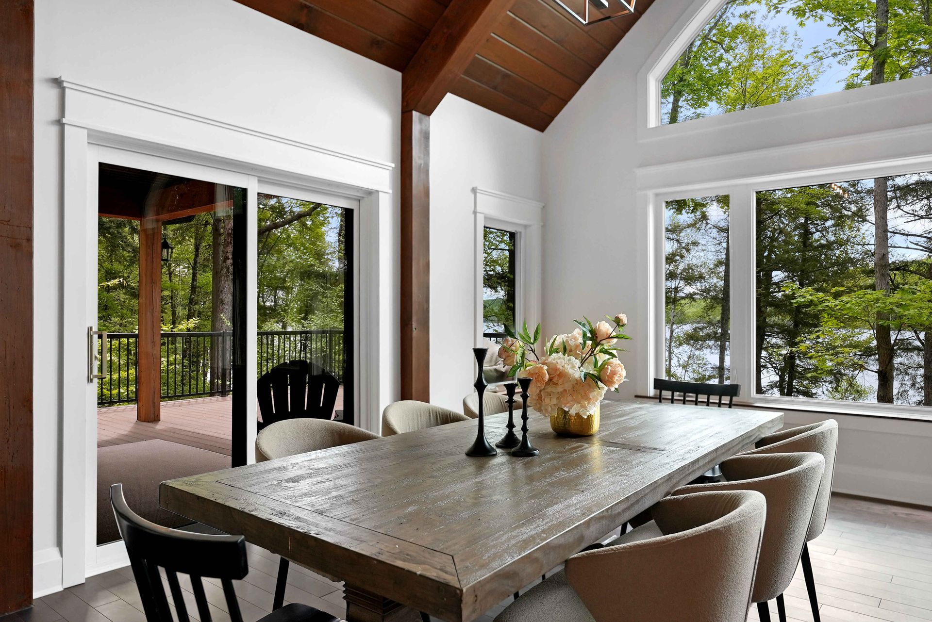Bright dining room with a large wooden table, beige chairs, and open doors to a tree-lined patio.