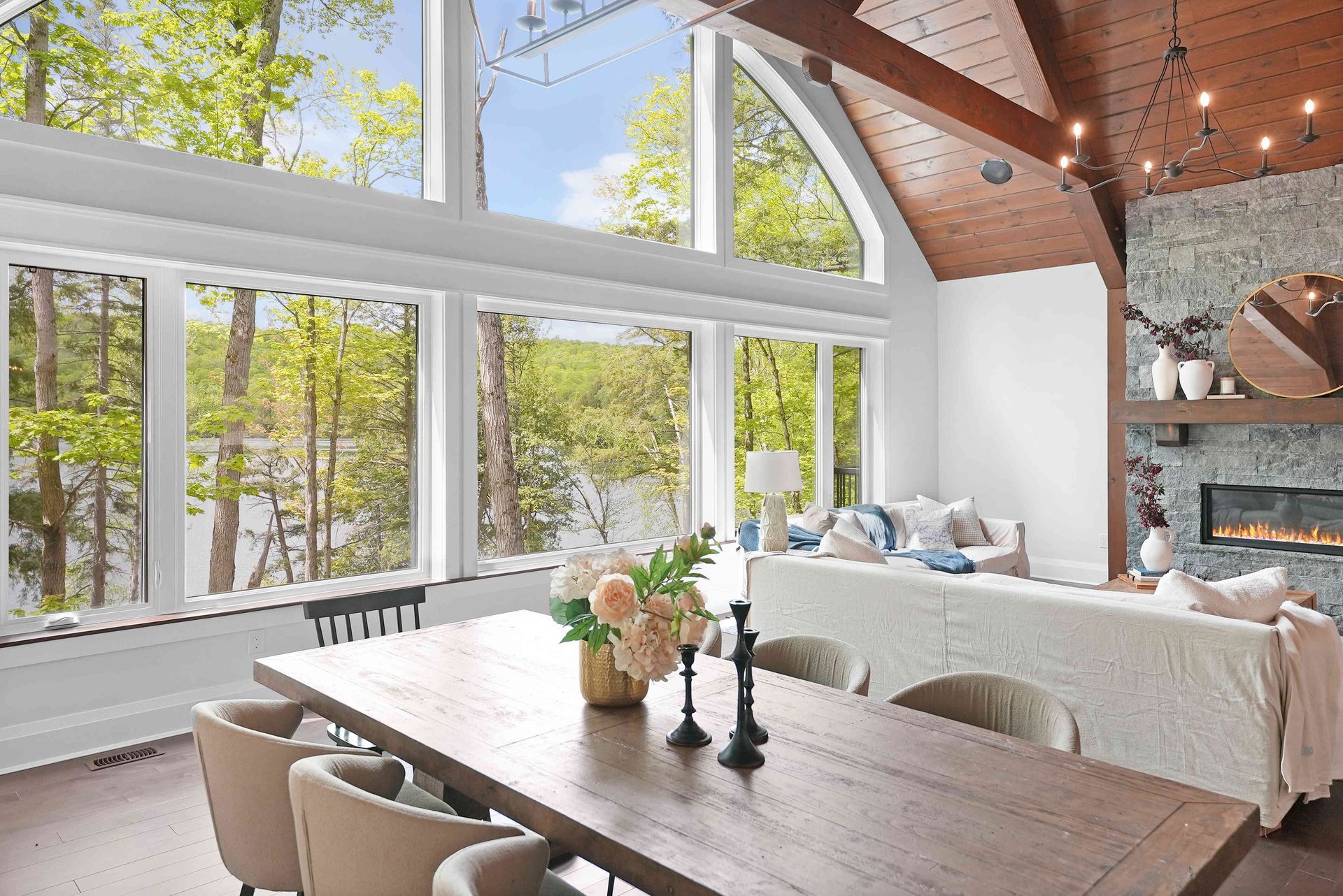 Bright, airy dining and living room with large windows, wood beams, and a sofa by a fireplace.