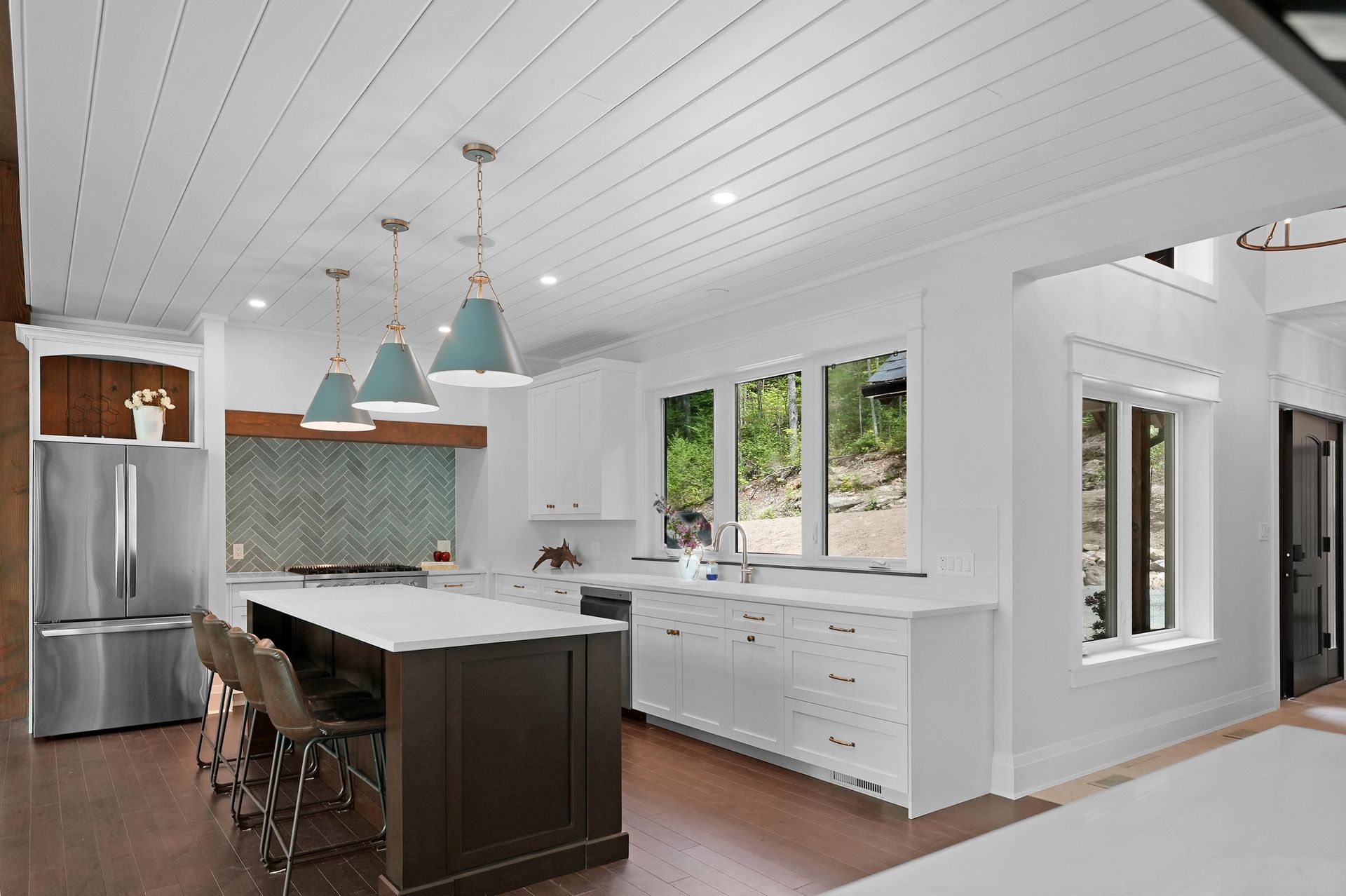 Bright modern kitchen with white cabinets, stainless fridge, island, pendant lights, and large windows