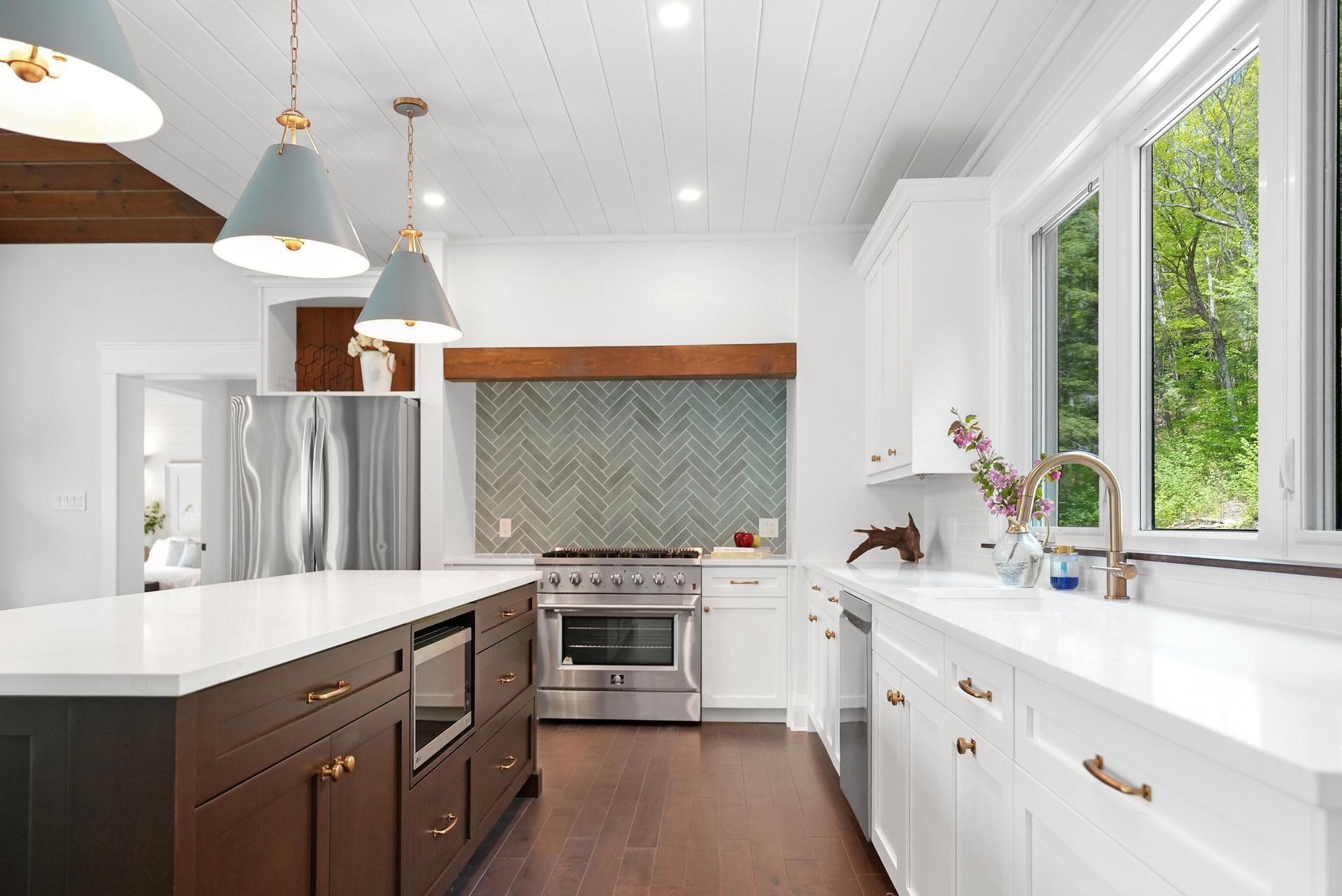 Bright modern kitchen with white cabinets, dark island, stainless stove, and large windows.