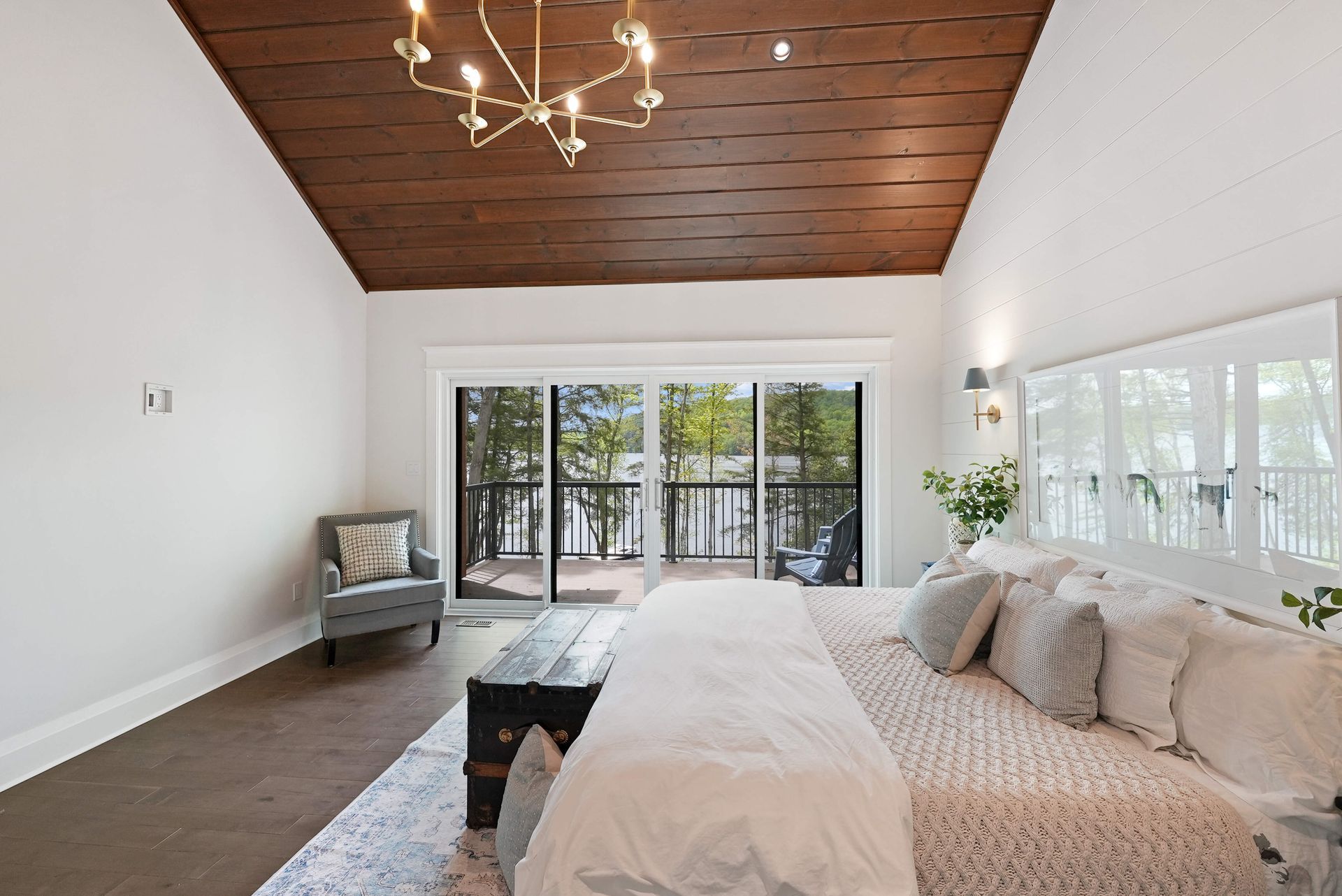 Spacious bedroom with white walls, wood ceiling, king bed, and sliding glass doors to a deck