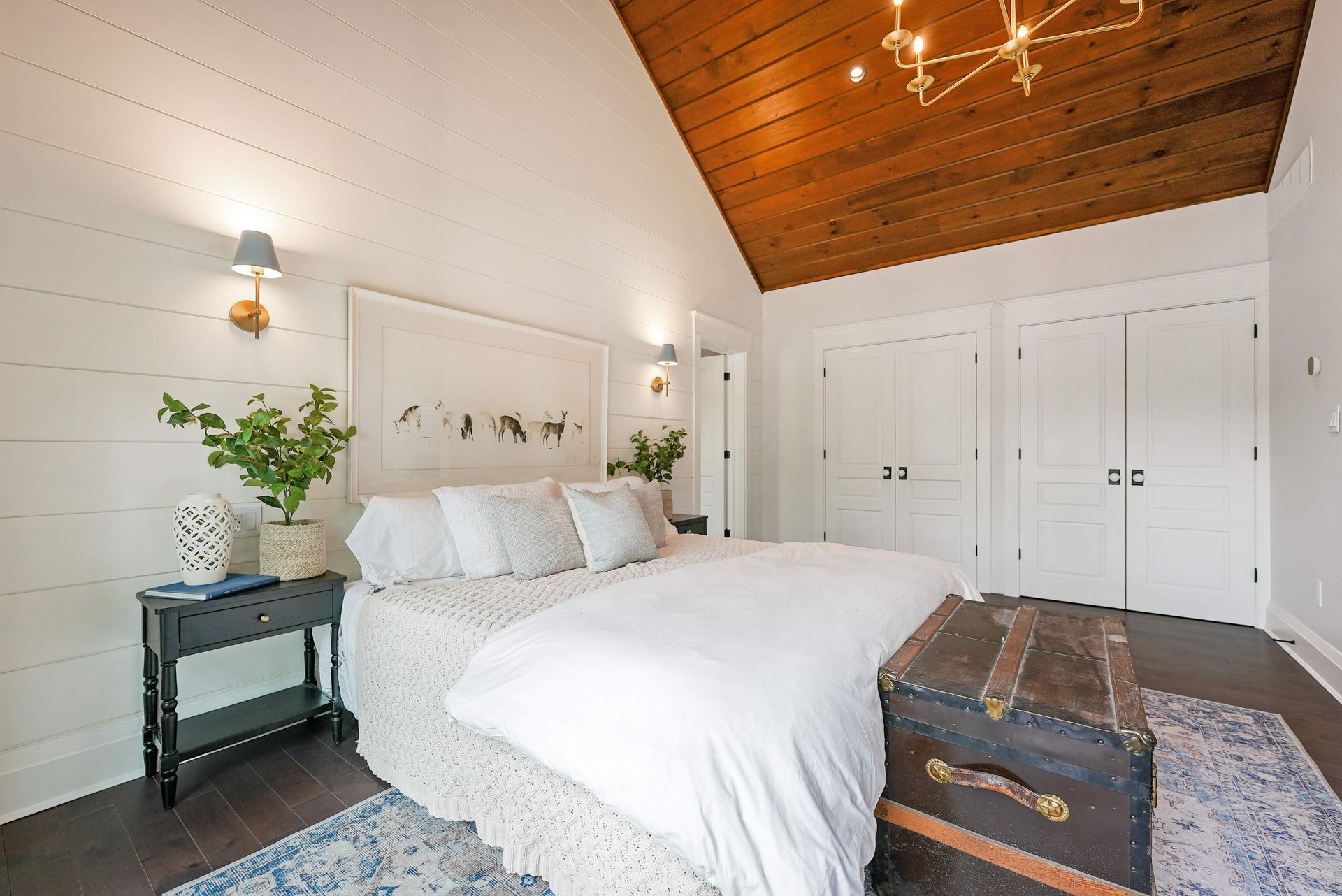 Bright bedroom with white bedding, wood ceiling, closet doors, and decorative trunk at the foot of the bed