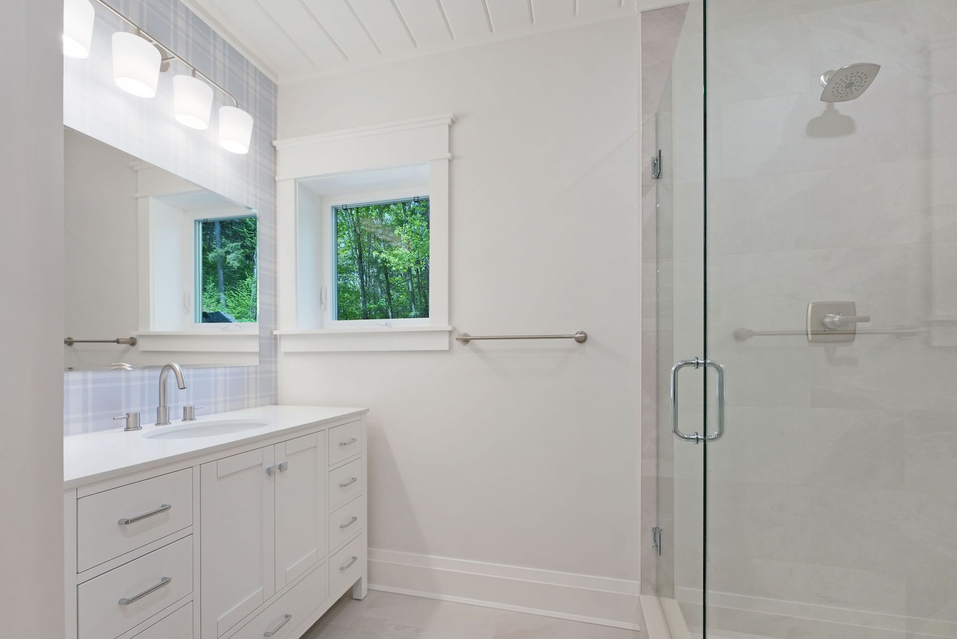 Bright white bathroom with vanity, window, and glass shower enclosure