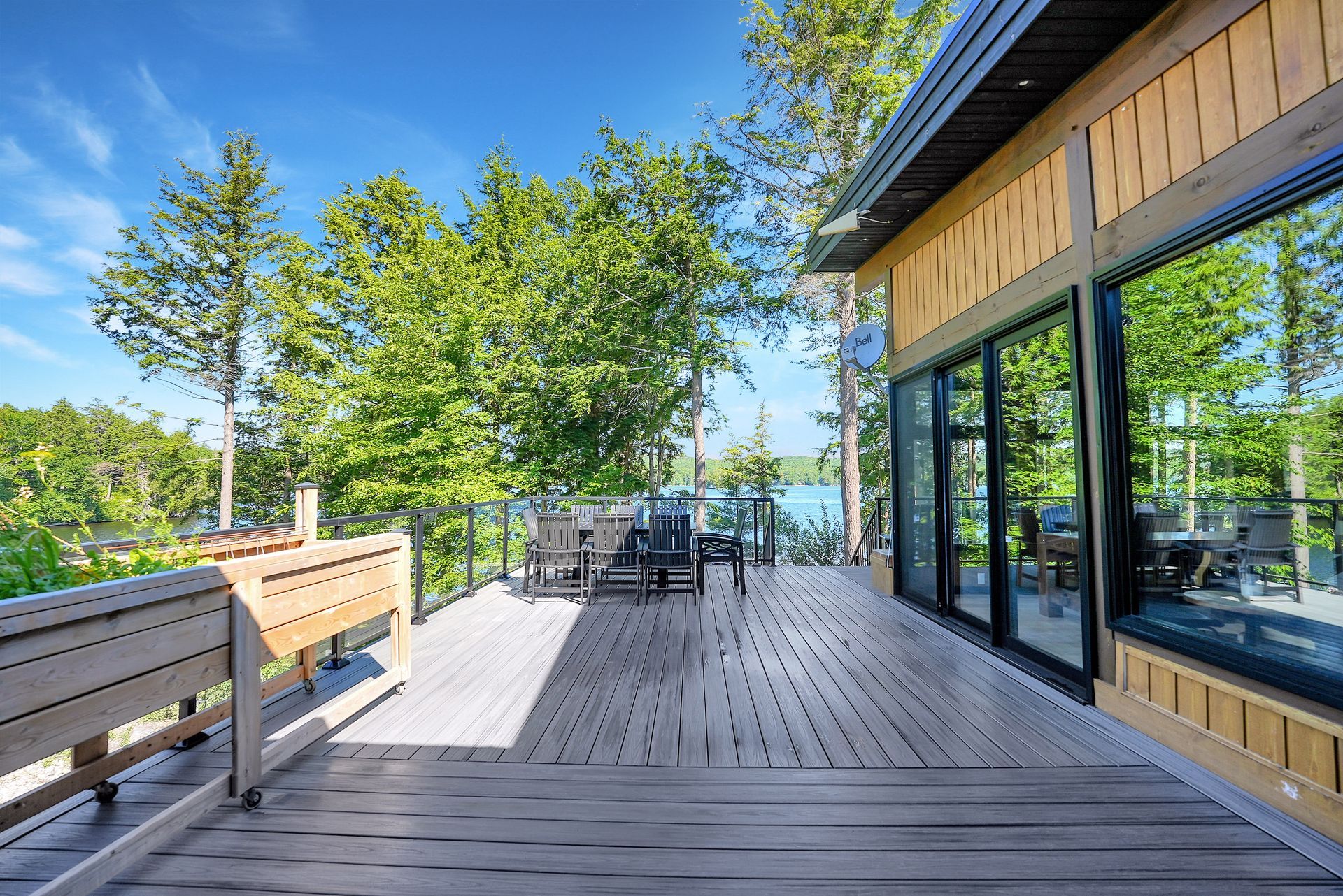 A patio with chairs and a table overlooking a lake in the woods.