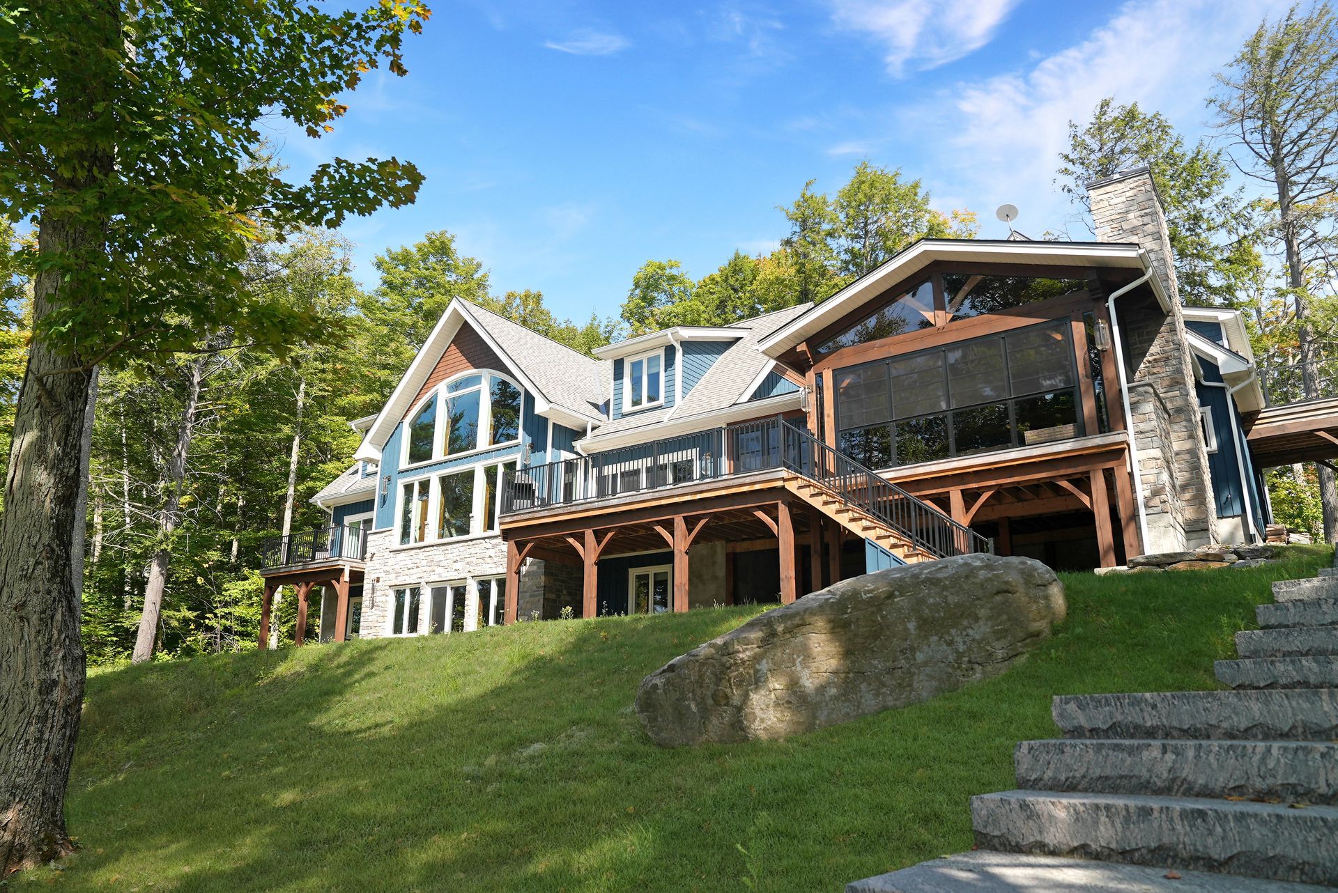 A large house with a wooden porch is surrounded by trees and bushes