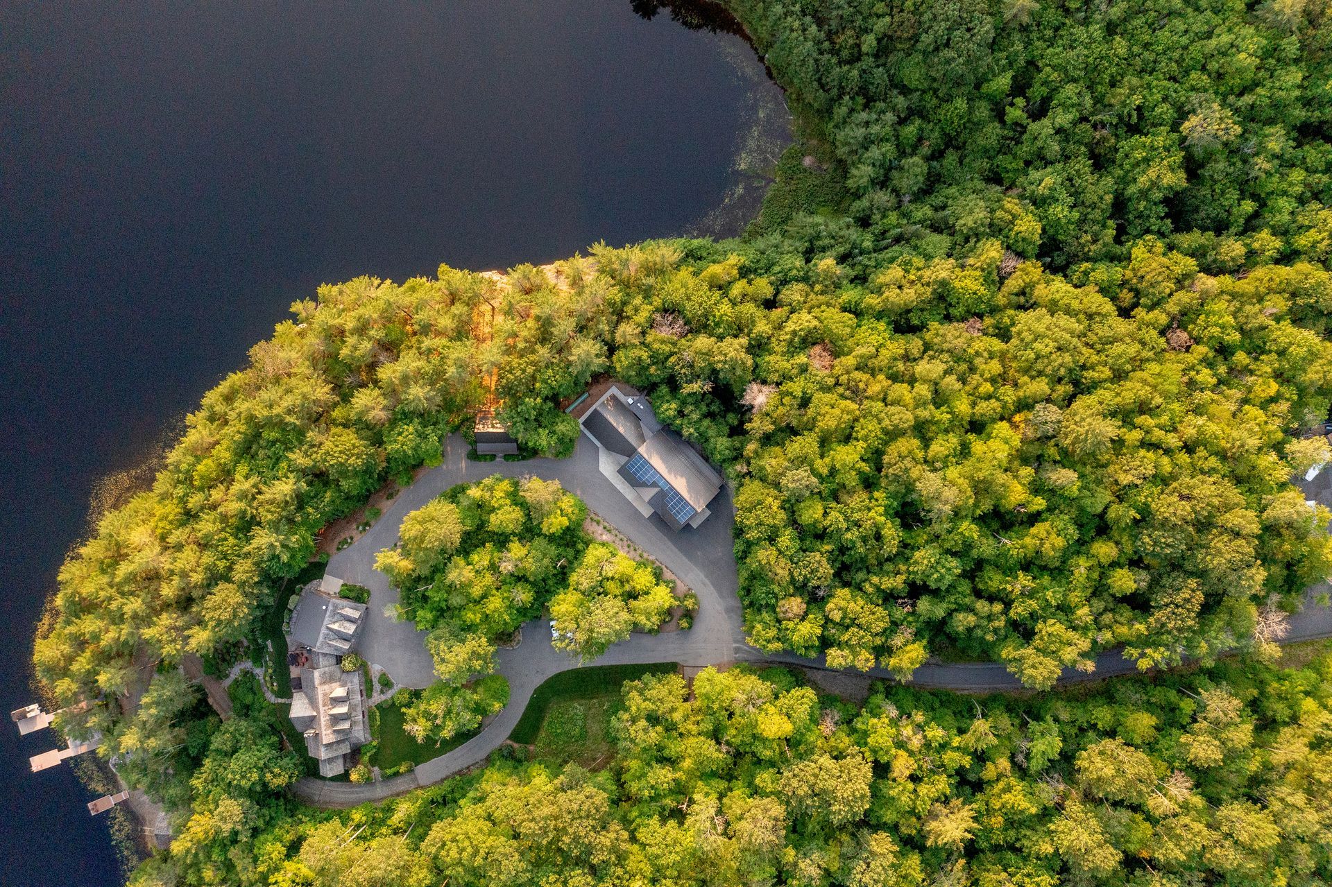 An aerial view of a house in the middle of a forest next to a lake.