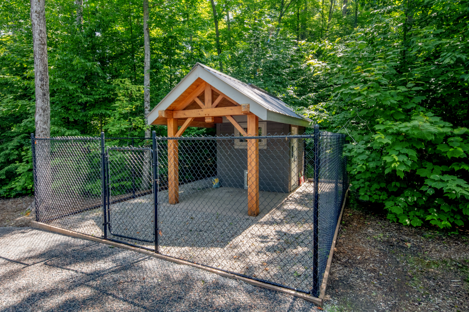 A small shed with a wooden roof is behind a chain link fence.