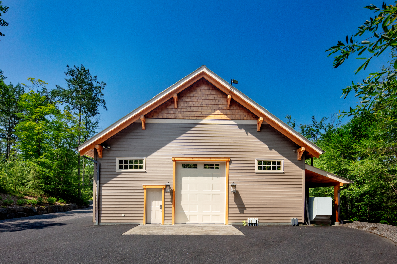 A large barn with a white garage door is surrounded by trees.