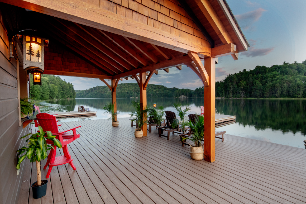 A wooden deck with chairs and a lantern overlooking a lake.