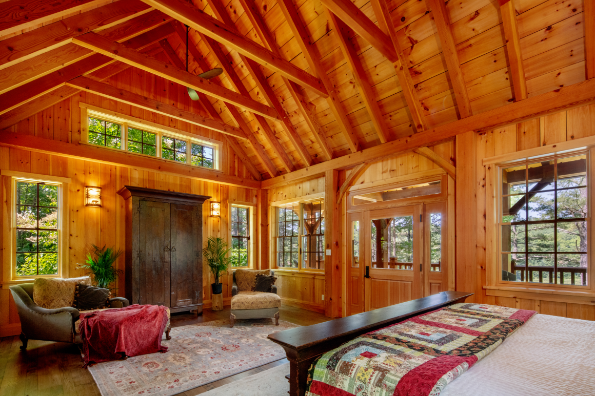 A bedroom in a wooden cabin with a bed , chairs , and windows.