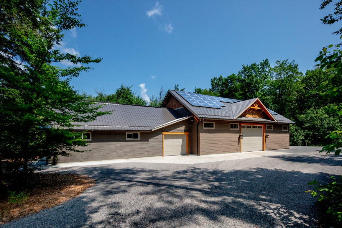 A large house with a garage and solar panels on the roof is surrounded by trees.