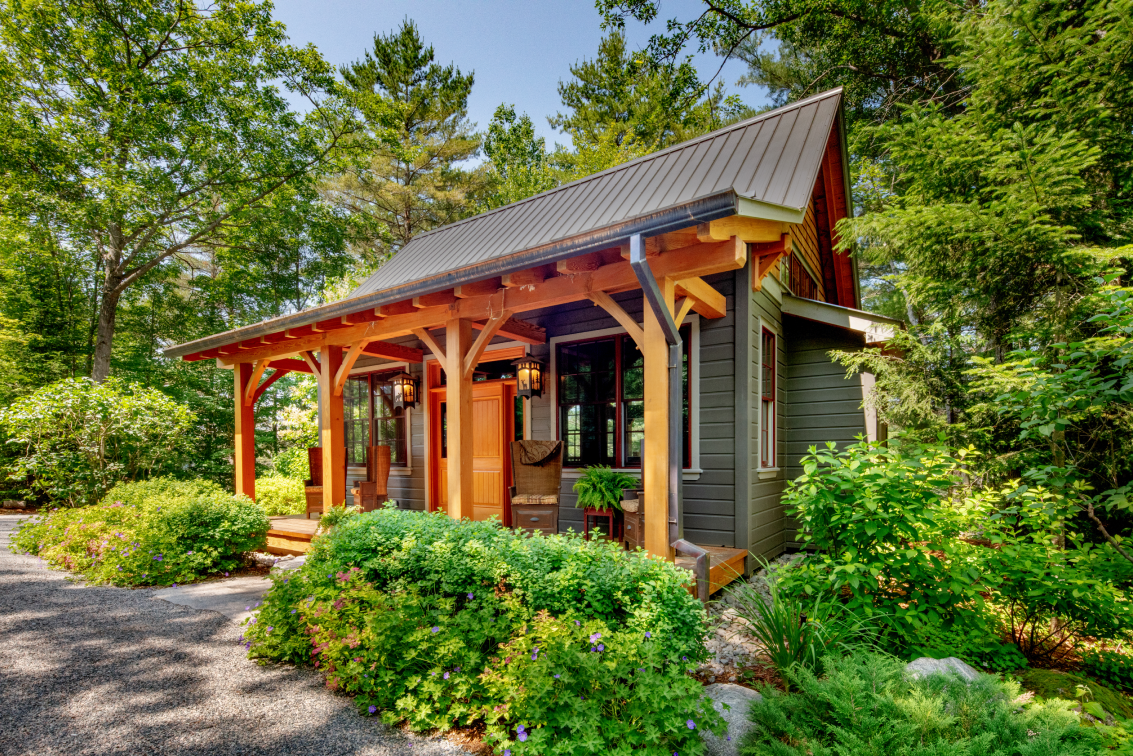 A small house with a porch in the middle of a forest.