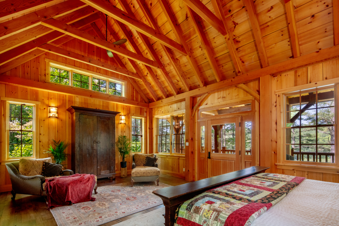 A bedroom in a wooden cabin with a bed , chairs , and a rug.