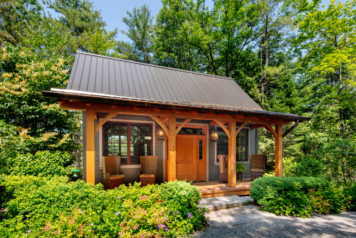 A small house with a metal roof is surrounded by trees.