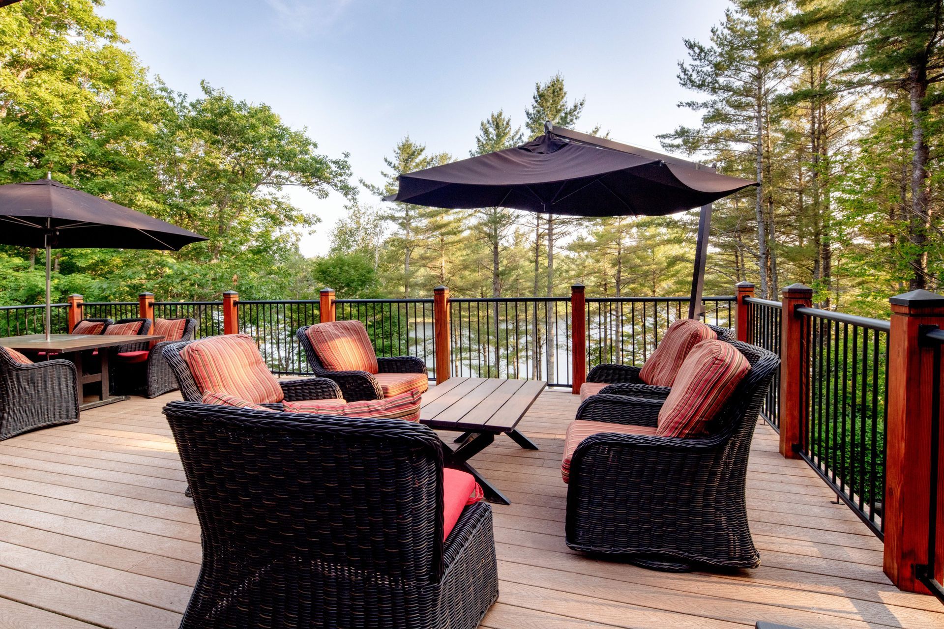 A deck with wicker furniture and umbrellas overlooking a lake