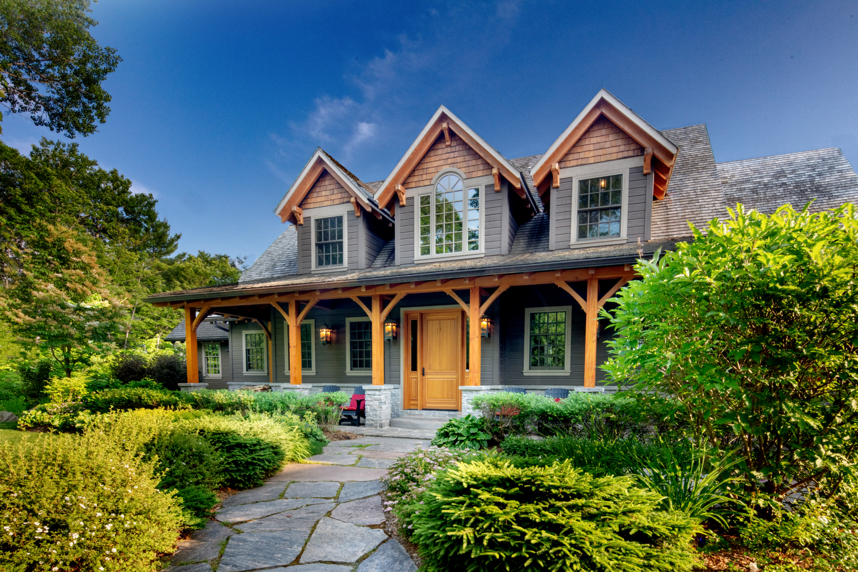 A large house with a wooden porch is surrounded by trees and bushes