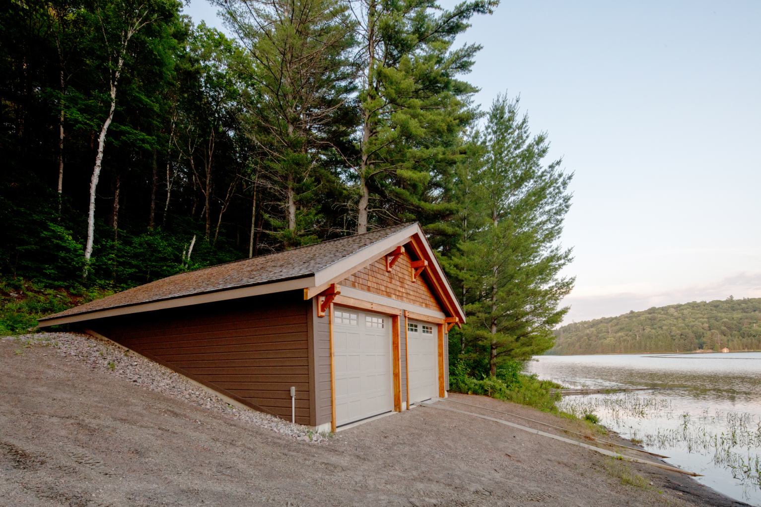A wooden garage is sitting next to a lake in the woods.