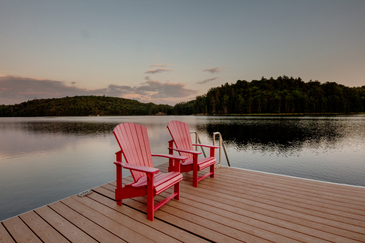 Two red adirondack chairs are sitting on a dock overlooking a lake.