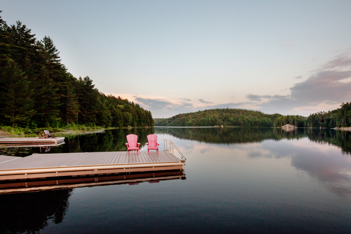 Two pink chairs are sitting on a dock overlooking a lake.