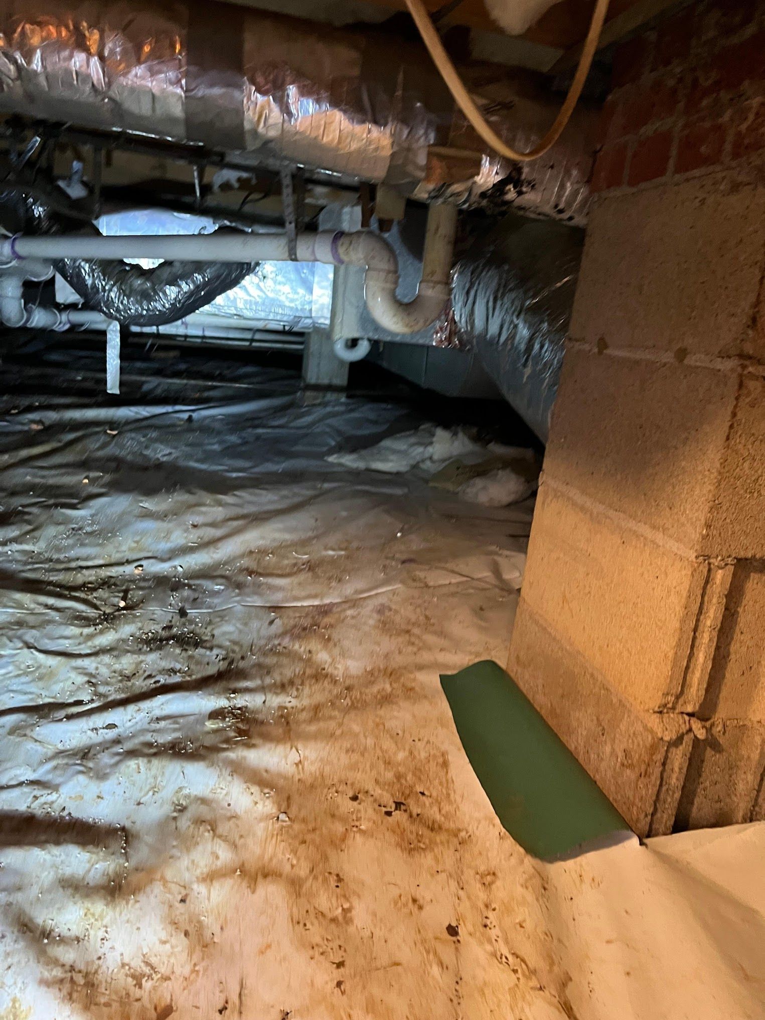 A dirty basement with a lot of pipes and a brick wall.