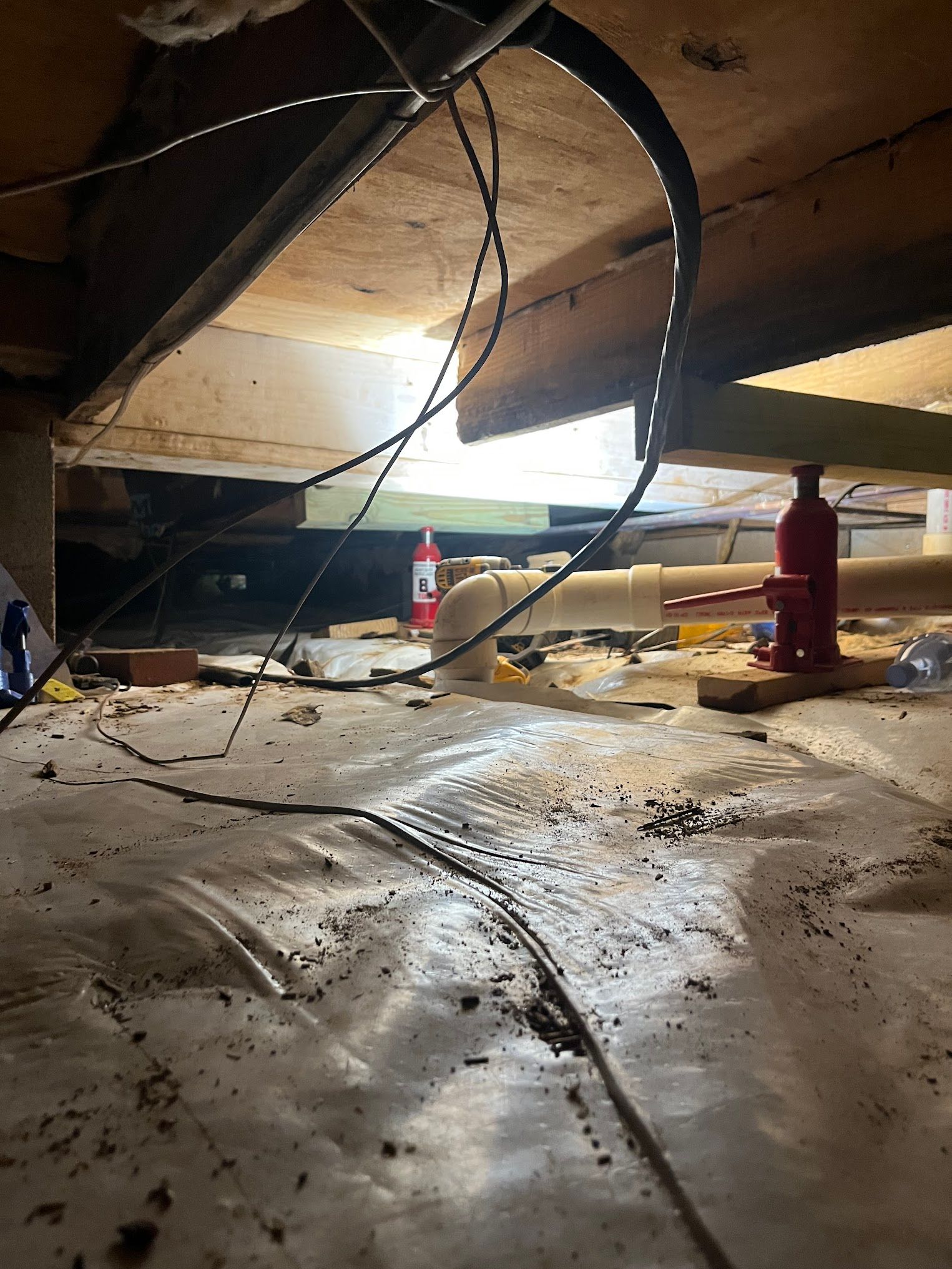 A red hydraulic jack is sitting under a wooden floor in a basement.