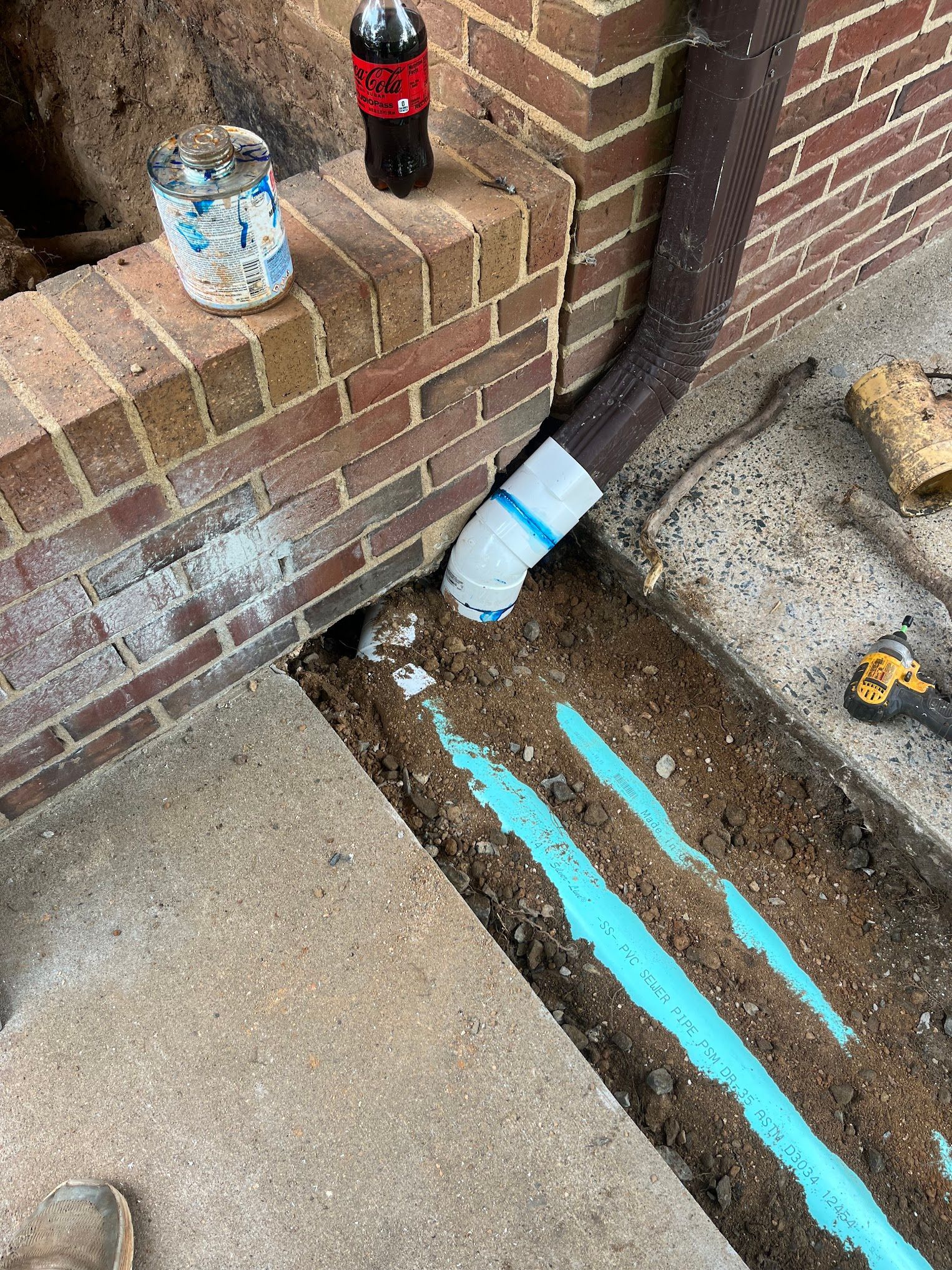 A drain pipe is being installed next to a brick wall.