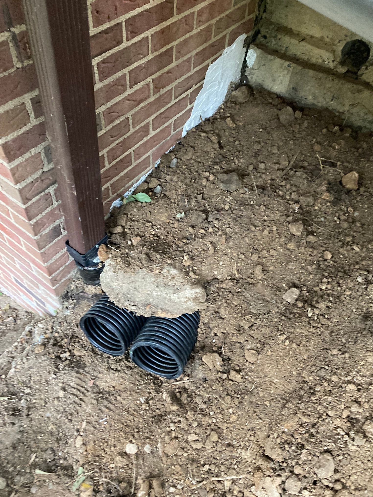 A drain pipe is sitting in the dirt next to a brick wall.
