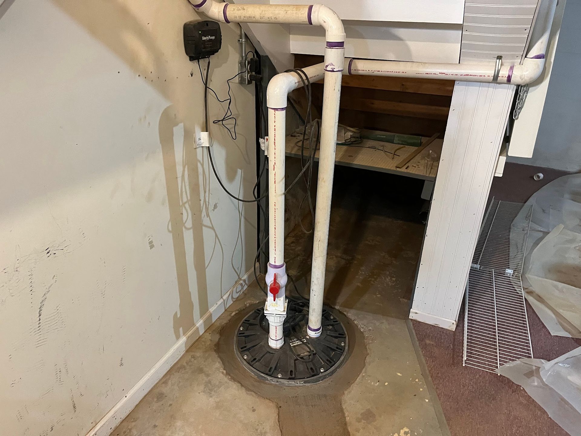 A basement pump is sitting on the floor next to a wall.