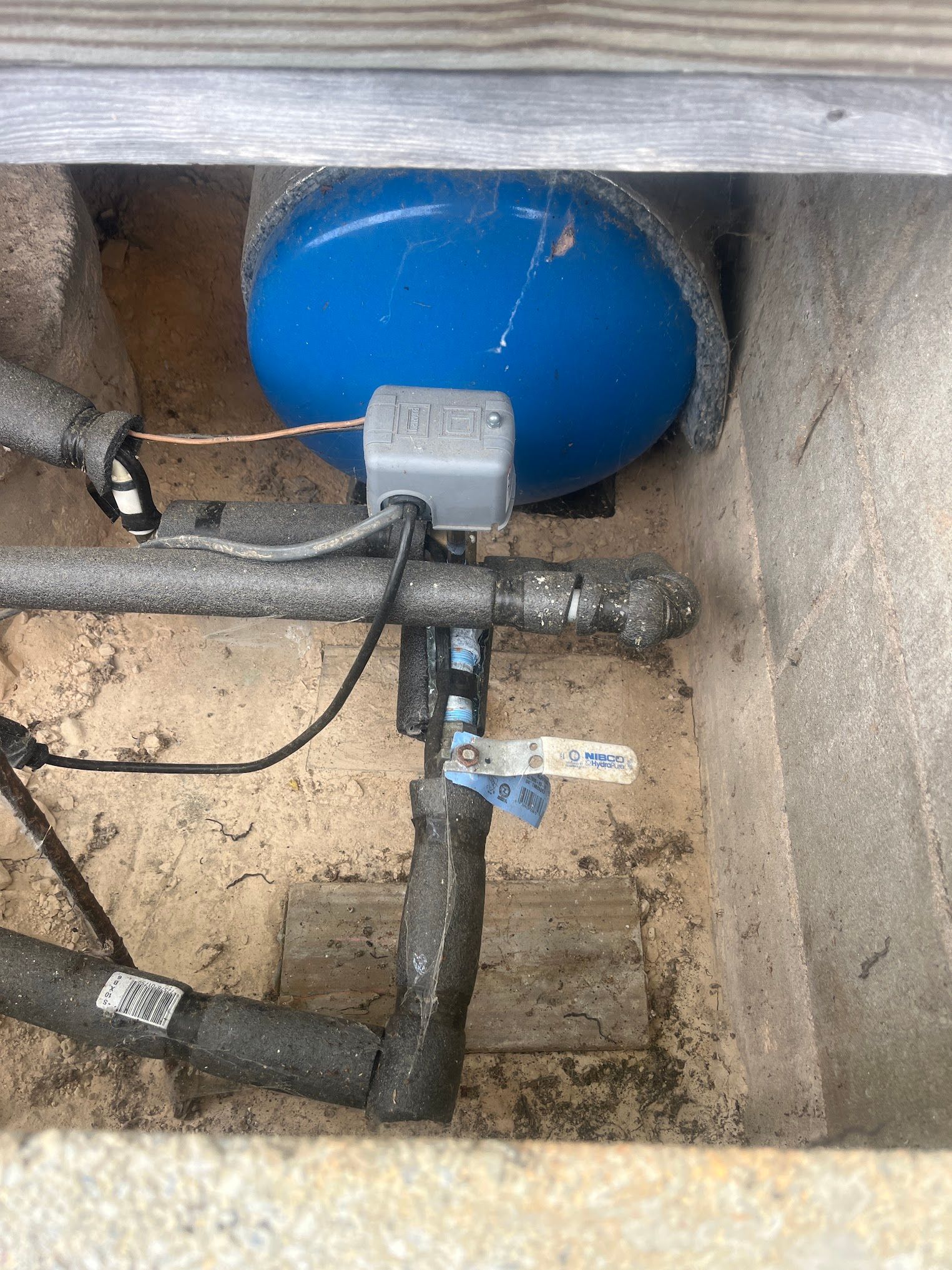 A blue water tank is sitting in a hole in the ground next to a valve.