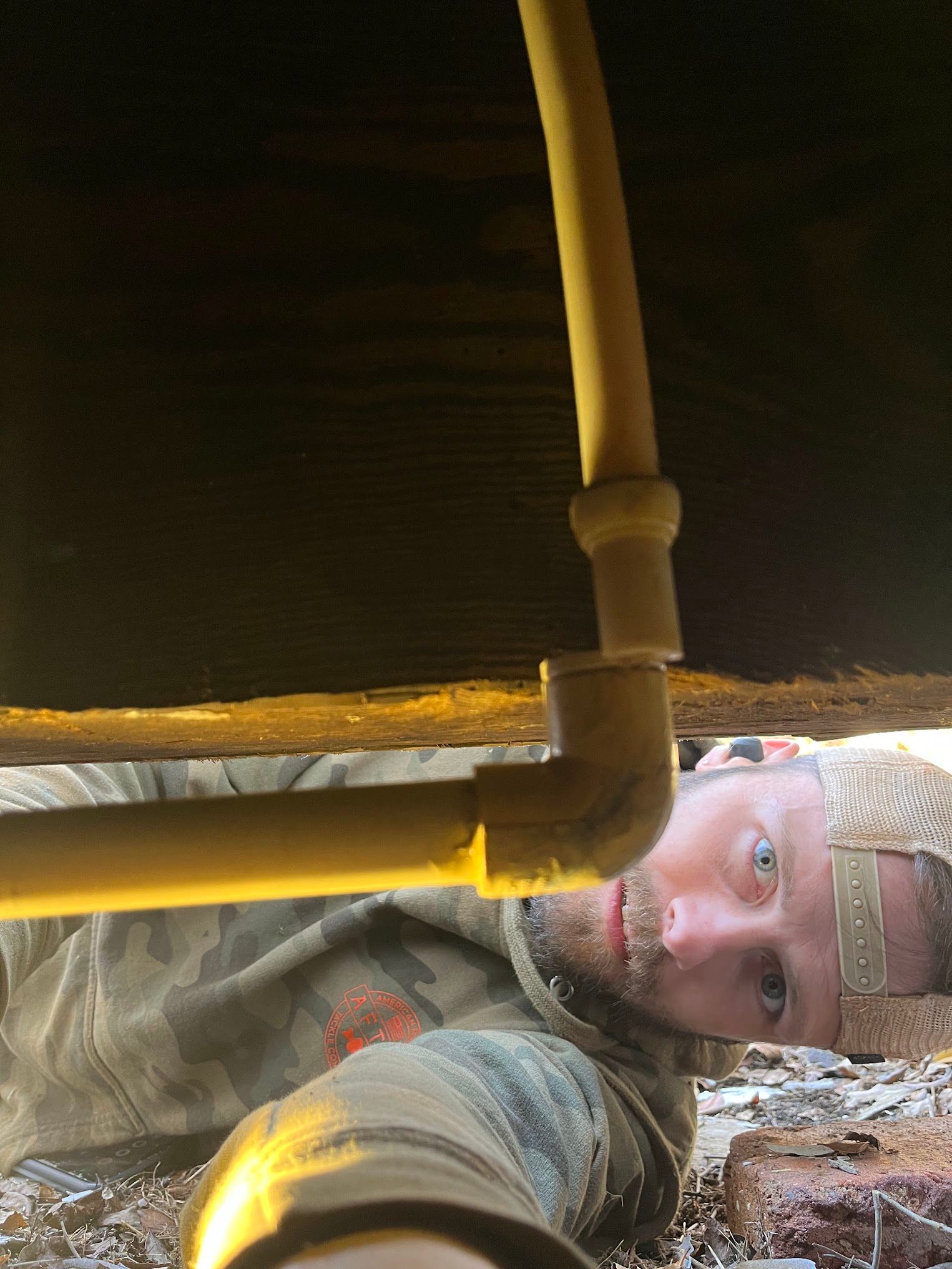 A man is laying on the ground under a pipe.