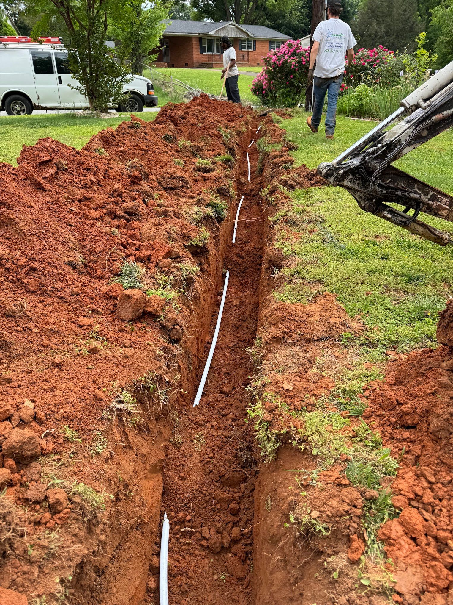 A man is digging a trench in the dirt in a yard.