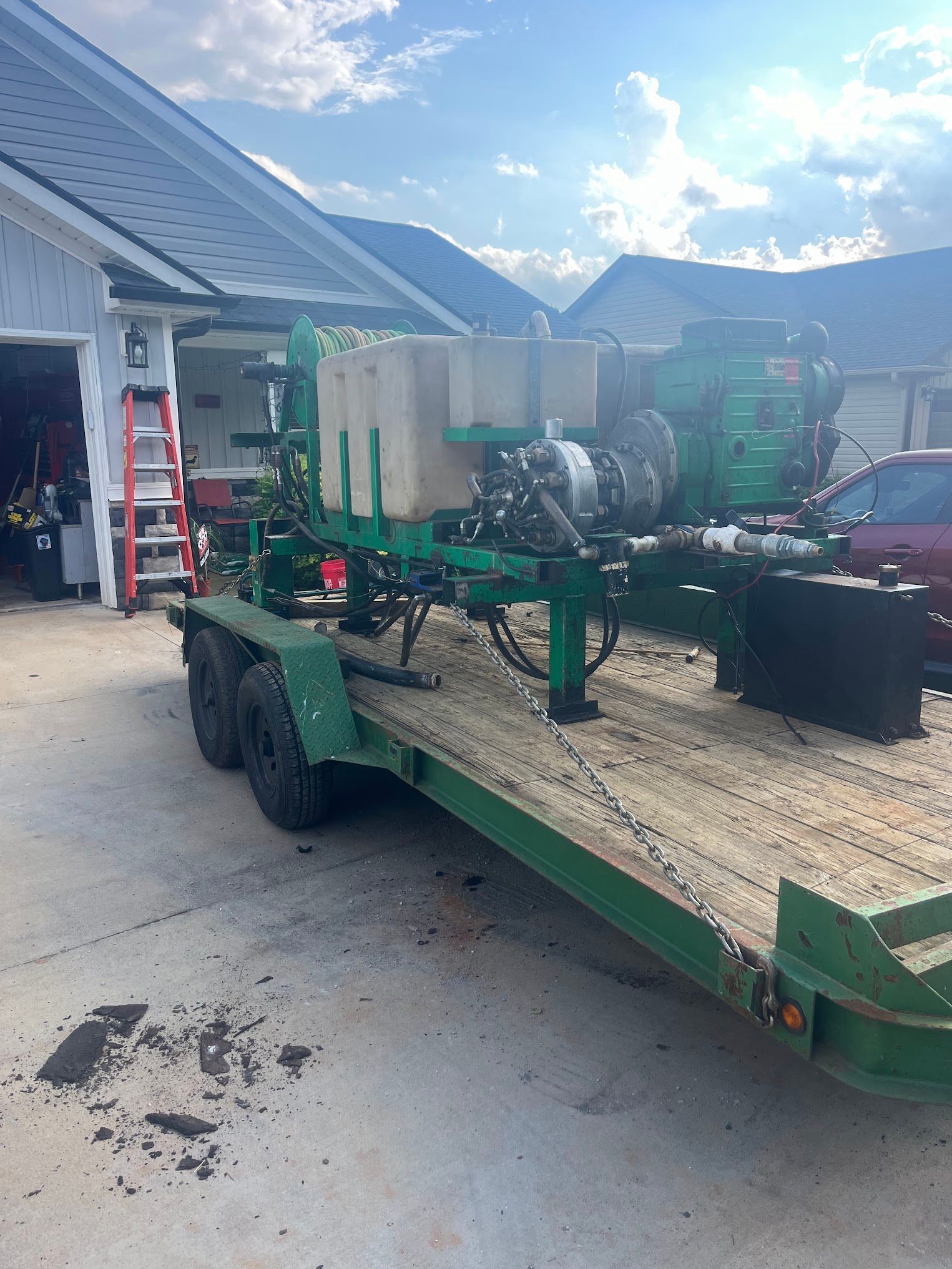 A green trailer with a machine on it is parked in front of a house.