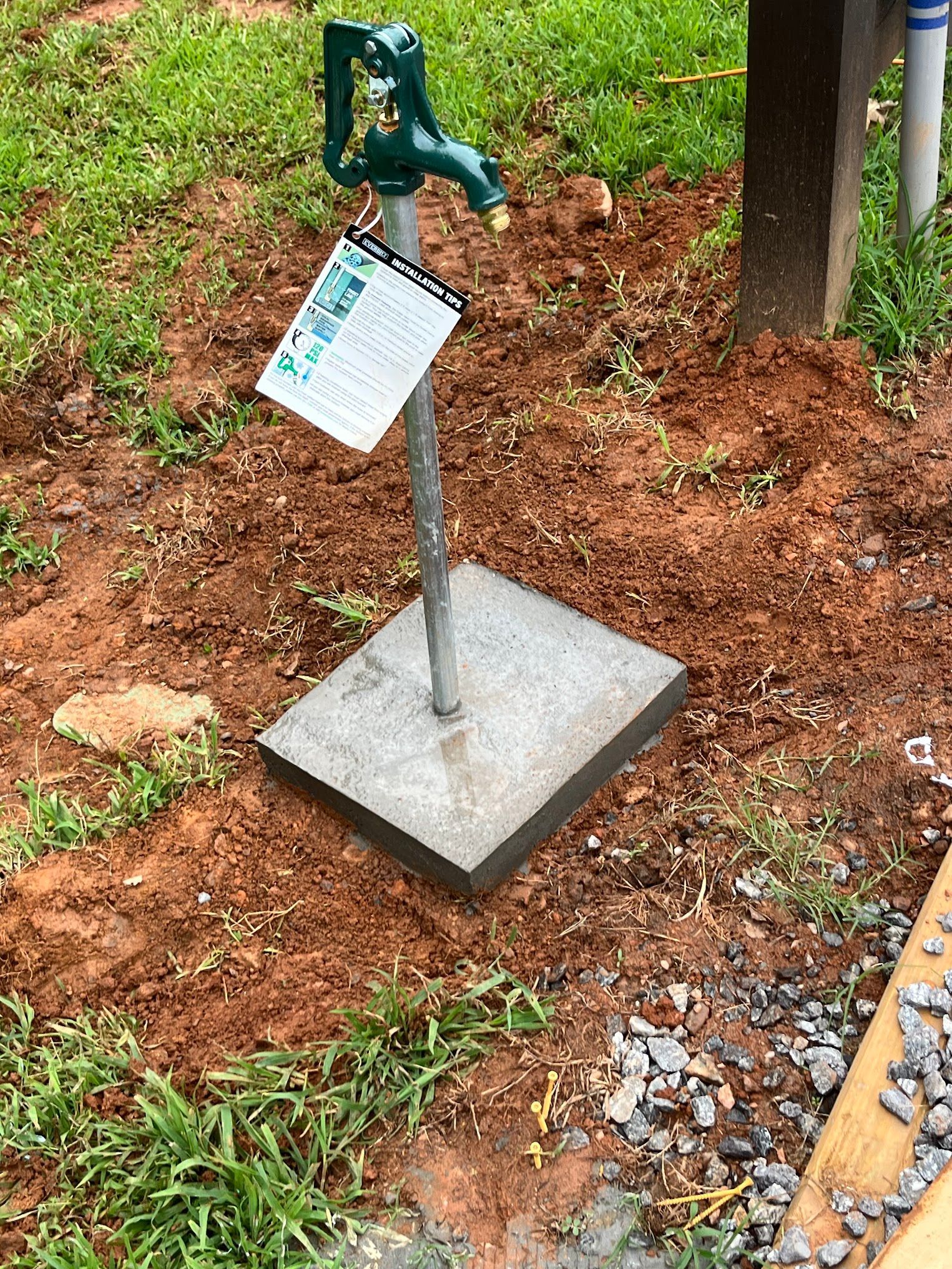 A green faucet is sitting on top of a concrete base in the dirt.